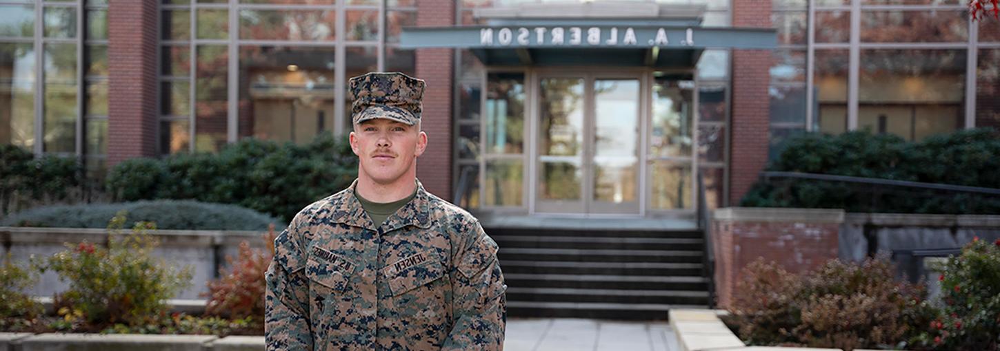 Man wearing battle dress uniform stands in front of Albertson’s Building